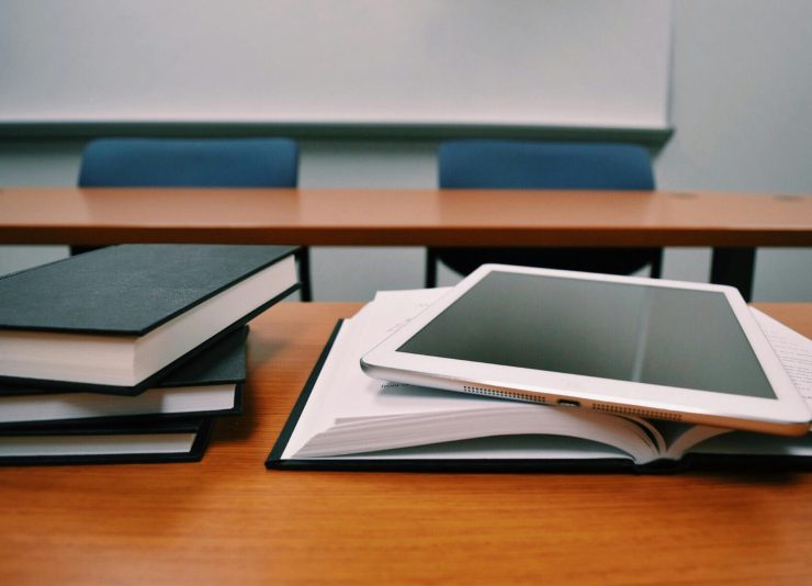 Books and a tablet on a desk in a classroom, depicting modern education.